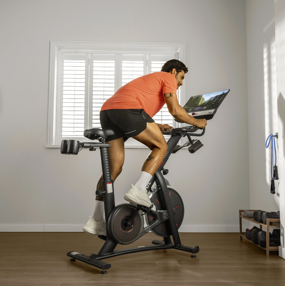 Man exercising on a stationary bike in a home setting with a laptop on the bike's console.
