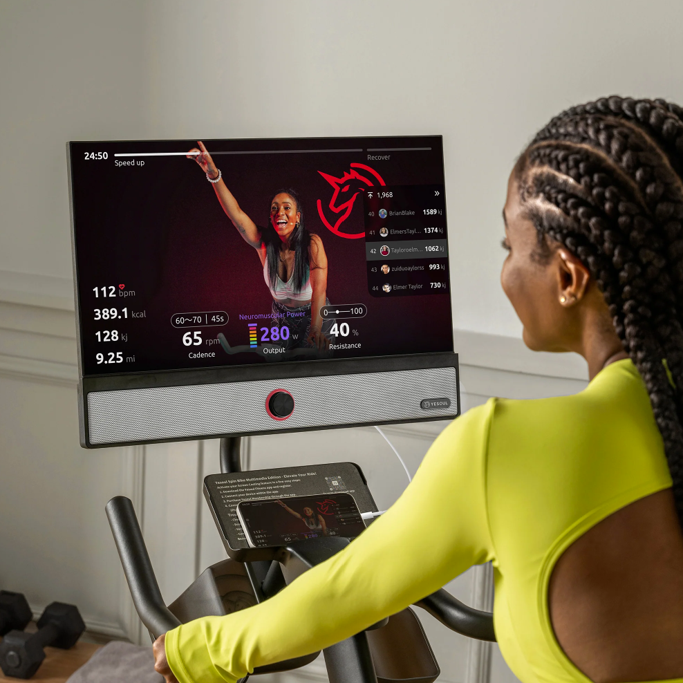Woman using a fitness machine with a screen displaying workout data in a home setting.