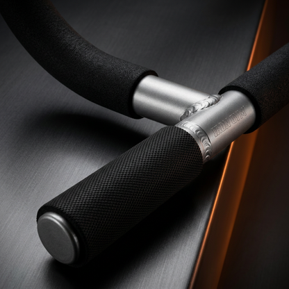 Close-up of a black foam exercise bar with textured black handles and silver metal ends on a dark brushed surface.